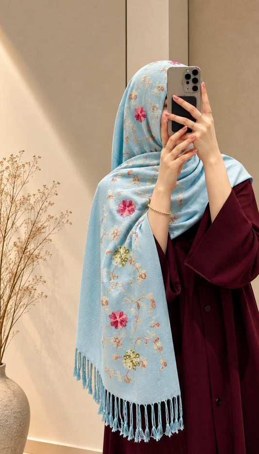 Ice blue cashmere embroidered hijab with pink and green floral details, delicate sequin embellishments, and matching fringed edges by Aynn Alif