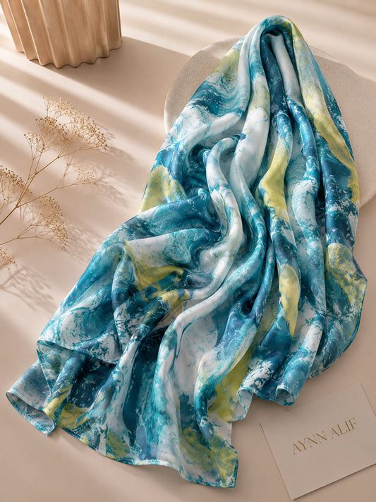 Extra large modal lawn hijab featuring an abstract watercolor print in aqua blue, teal, ivory and soft lime tones, styled in an elegant draped flatlay.