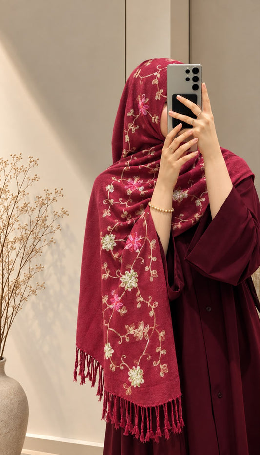 Berry red cashmere embroidered hijab with floral sequin embellishments and fringed edges by Aynn Alif, styled with a maroon abaya.