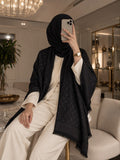 Black monogram-inspired pashmina wrap with tonal pattern, wide border and fringed edges, styled as an elegant winter layer for women.