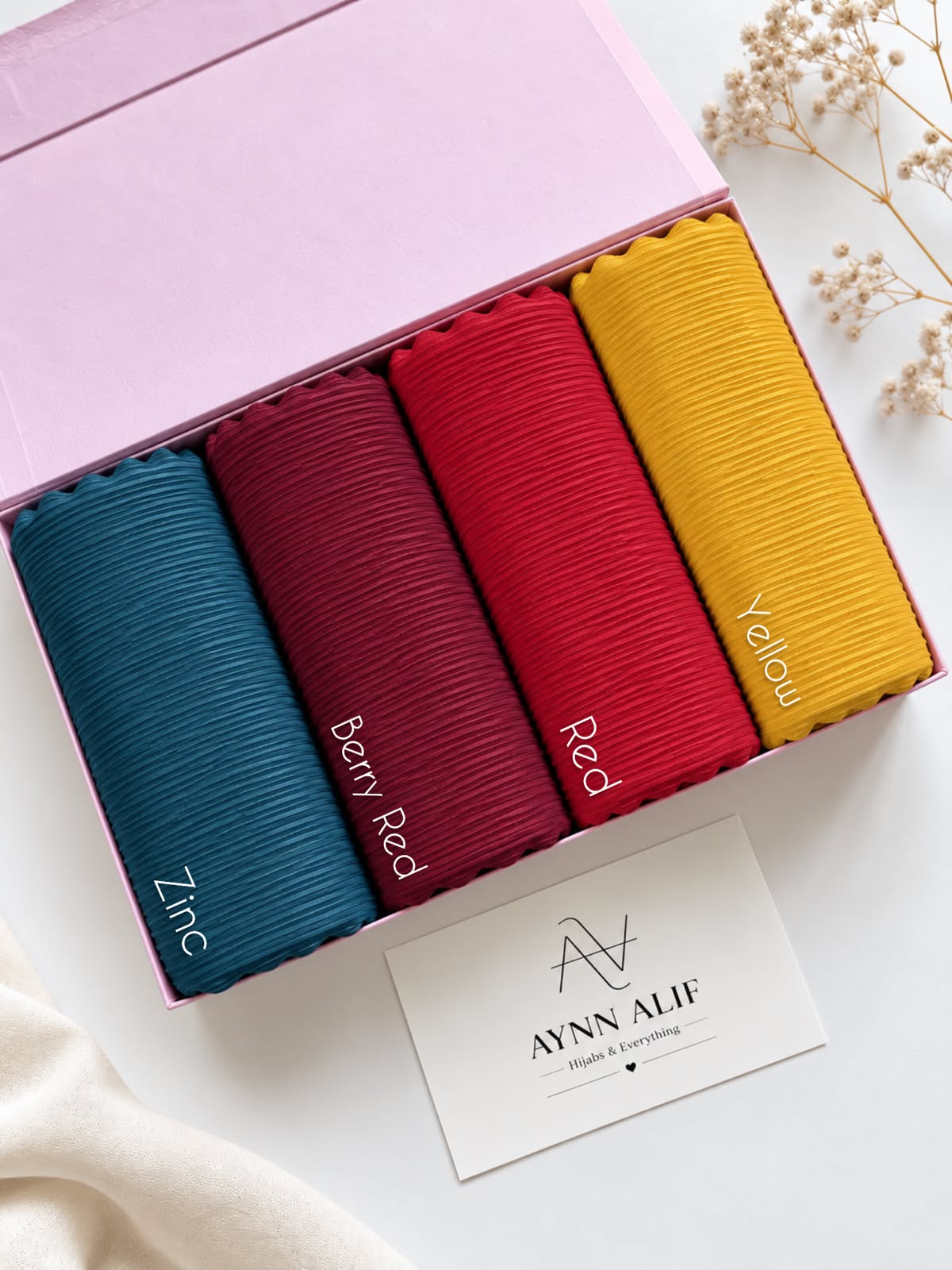 Aynn Alif ribbed jersey hijabs in Zinc, Berry Red, Red and Yellow arranged in a pink box