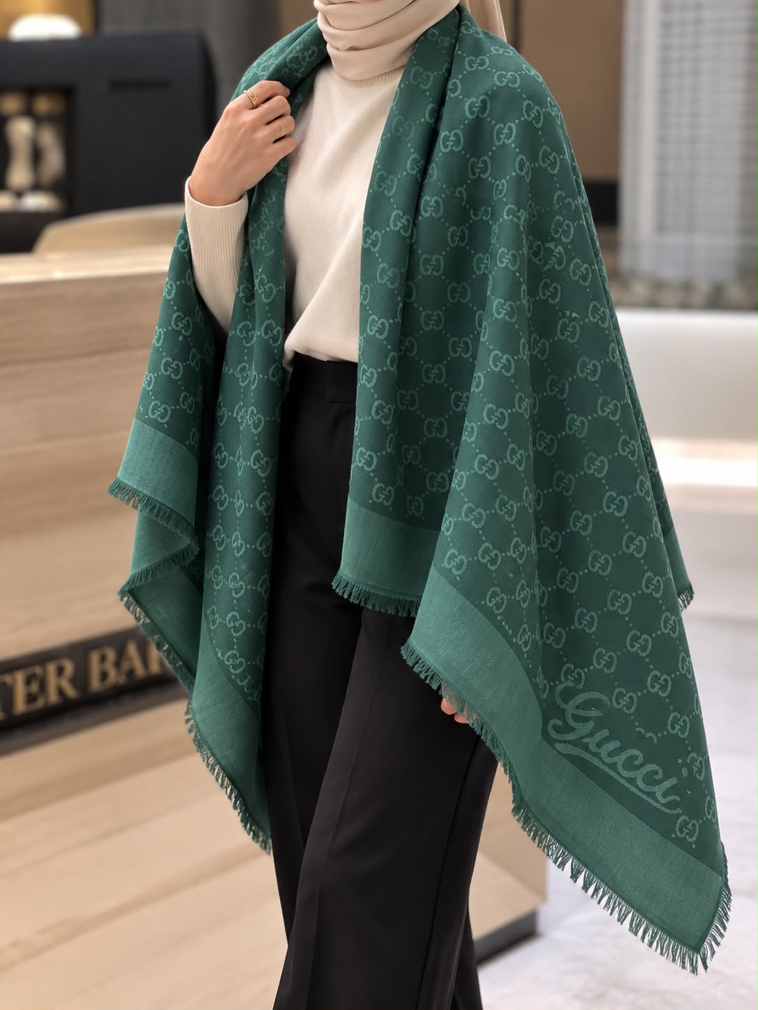 Emerald green monogram-inspired pashmina wrap with tonal detailing, coordinating border and fringed edges styled for elegant winter layering.