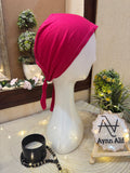A mannequin head wearing a pink tie back hijab cap with a branded sign reading 'Ayn Alif' in the background.