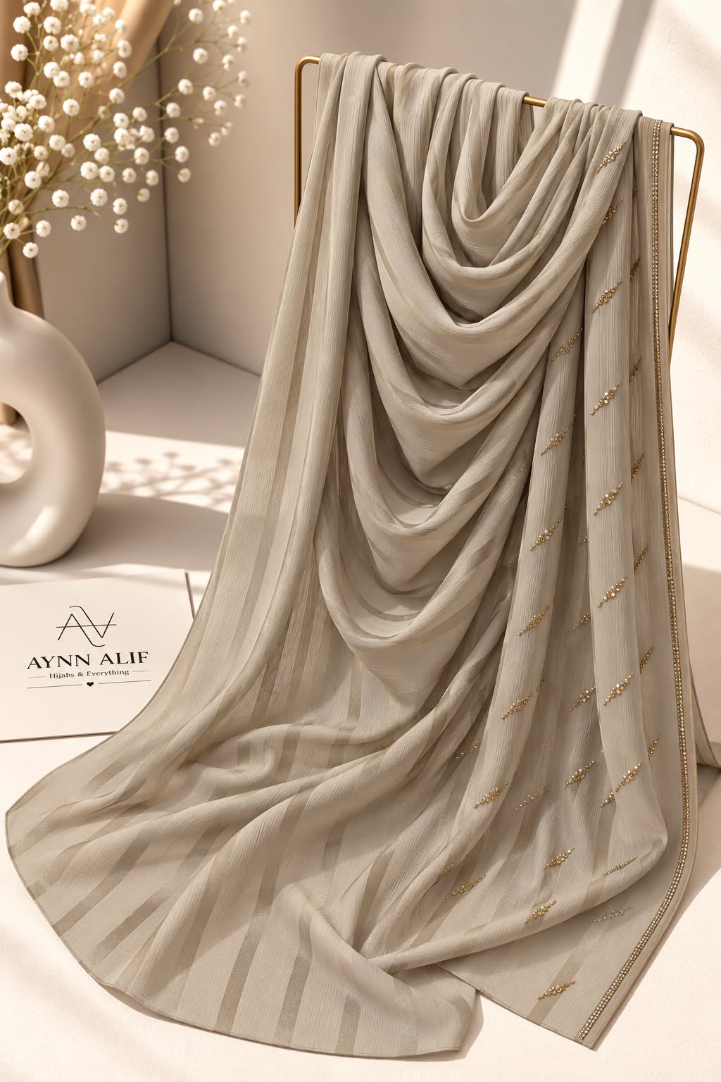 
Khaaki crinkle chiffon georgette hijab with satin stripes and delicate stone-studded detailing by Aynn Alif.