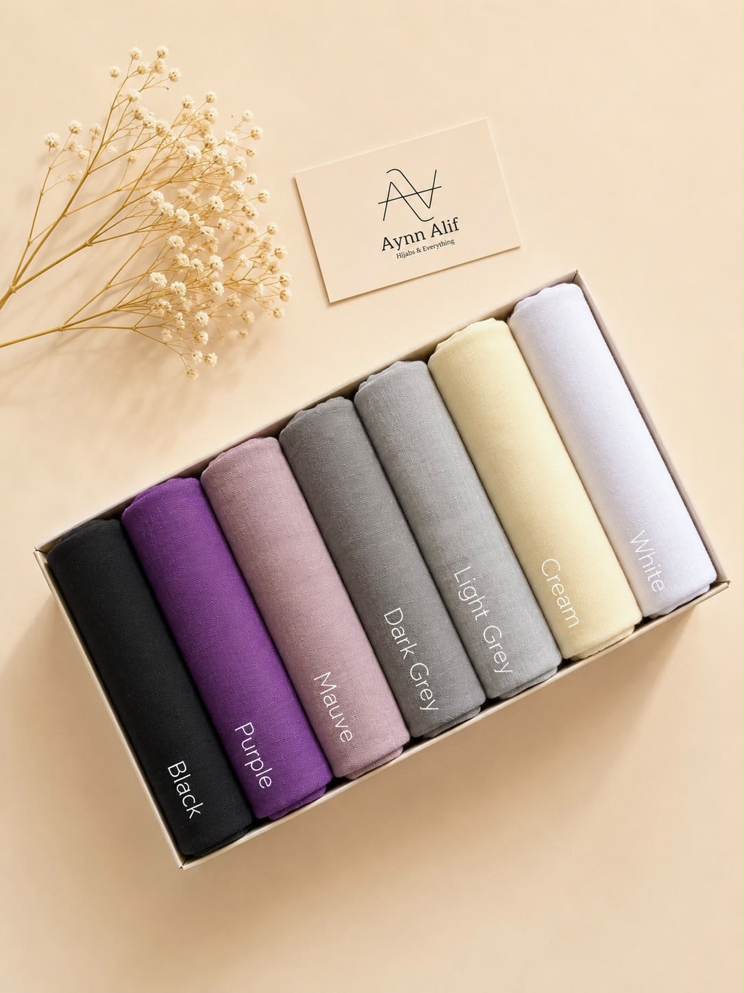 Large size Turkish lawn hijabs in Black, Purple, Mauve, Dark Grey, Light Grey, Cream, and White neatly arranged in a gift box by Aynn Alif.