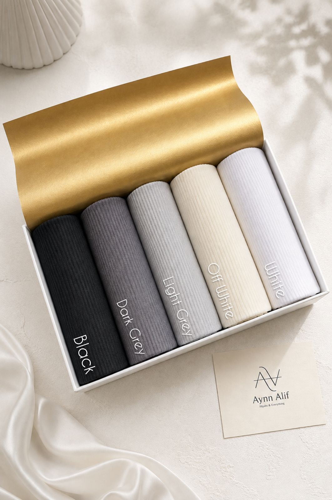 Ribbed jersey hijabs in black, dark grey, light grey, off white and white arranged in a white presentation box.