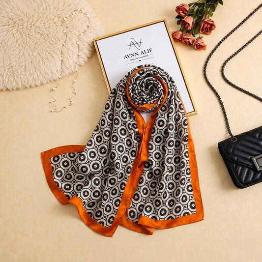 Black and ivory printed silk scarf with repeating geometric motifs and rich orange border by Aynn Alif