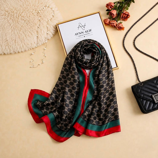 Black printed silk scarf with repeating monogram-inspired pattern and emerald green and deep red border on all four sides by Aynn Alif
