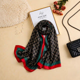 Black printed silk scarf with repeating monogram-inspired pattern and emerald green and deep red border on all four sides by Aynn Alif