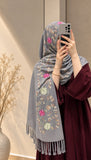 Silver grey cashmere embroidered hijab featuring pink and green floral motifs, delicate sequin embellishments, and matching grey fringed edges by Aynn Alif.